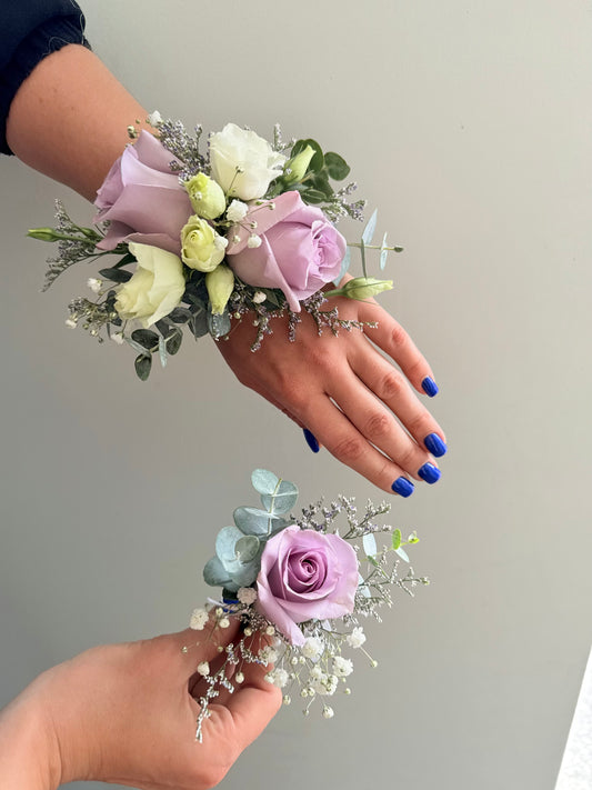 Two hands wearing wrist Boutonnière with pink and white flowers on a plain background