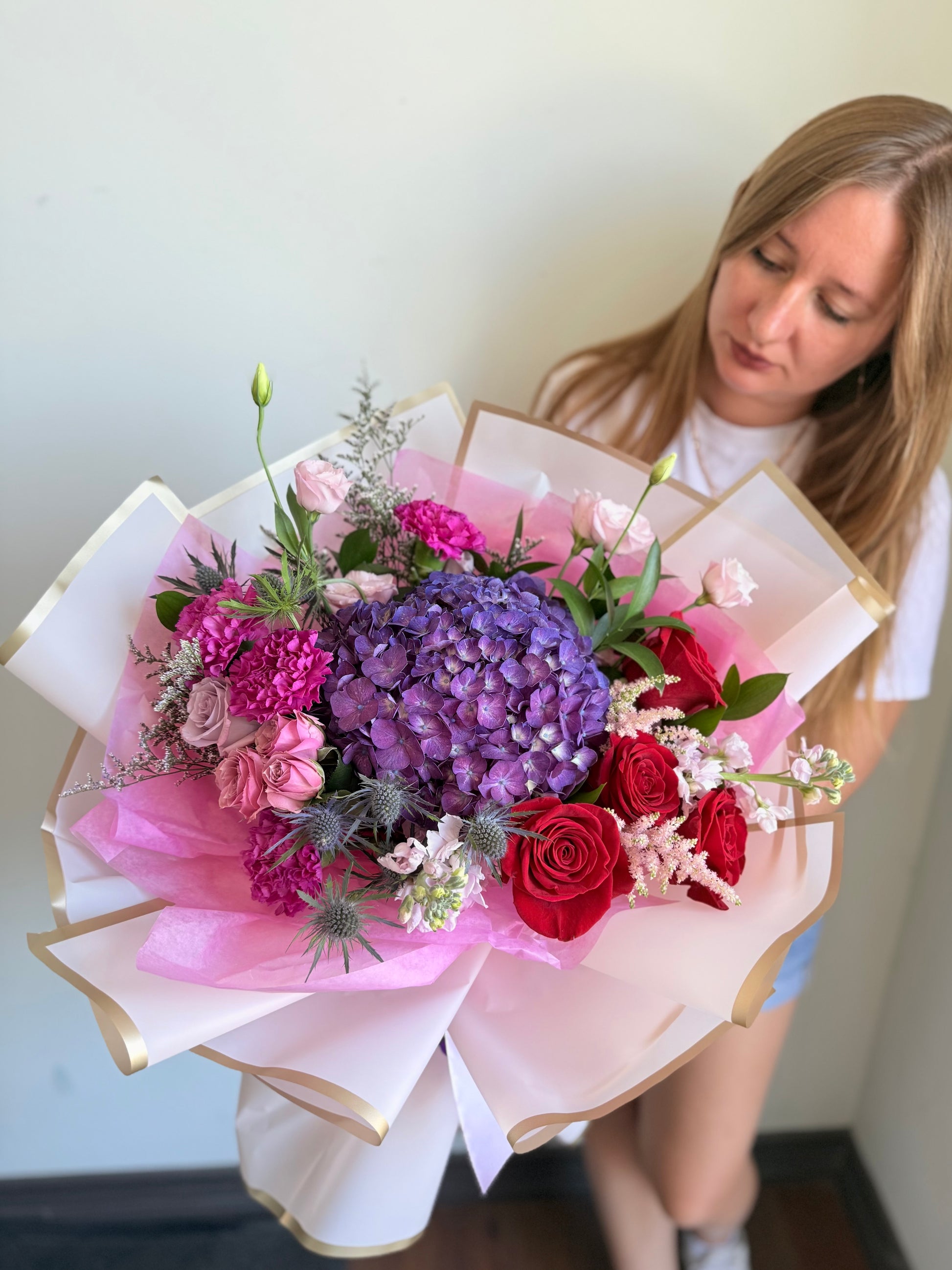 Woman holding a large Deeply Yours Bouquet of flowers wrapped in pink paper with gold edges.