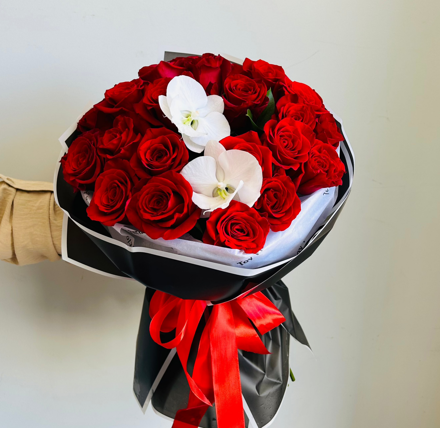 Bouquet of red roses with white orchids wrapped in black paper and red ribbon.