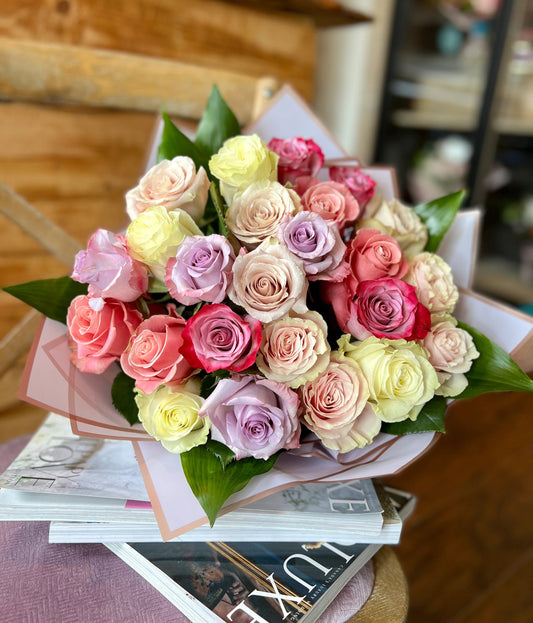 A bouquet of mixed roses in shades of pink, red, beige, and purple, arranged and wrapped with Toy Florist signature wrapping.