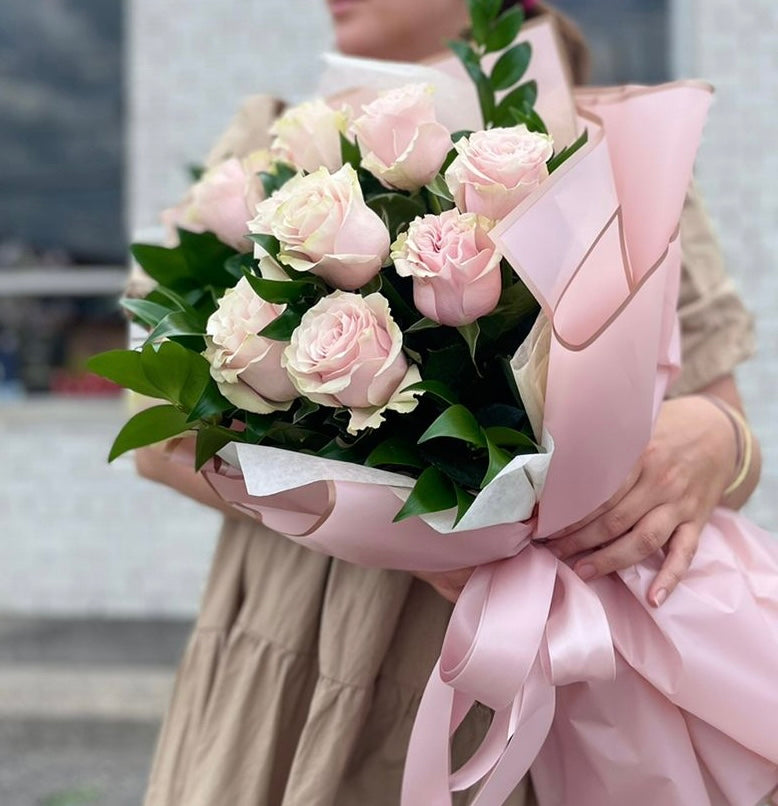 dozen light pink roses wrapped with pink paper and tied with a pink ribbon.